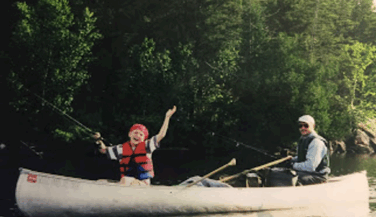 A boy throws up his arms in the front of an aluminum canoe